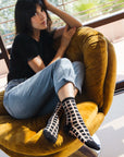 femme assise sur fauteuil jambes croisées avec chaussettes transparentes à carreaux noirs ambiance décontractée