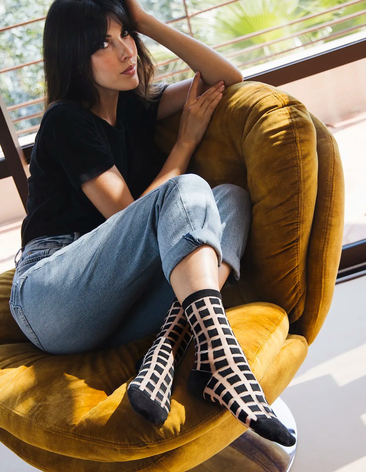 femme assise sur fauteuil jambes croisées avec chaussettes transparentes à carreaux noirs ambiance décontractée