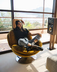 femme assise sur fauteuil dans une ambiance poétique avec paysage de mer en fond, tenue décontractée et chaussettes transparentes à carreaux noirs avec mocassins noirs