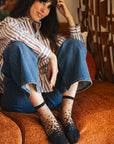 Chaussettes transparentes à pois noirs, portées par une femme assise sur un canapé portant un jean bleu et une chemise rayée