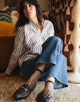 Chaussettes transparentes à pois noirs, portées par une femme assise par terre portant un jean bleu, une chemise rayée et des mocassins bordeaux